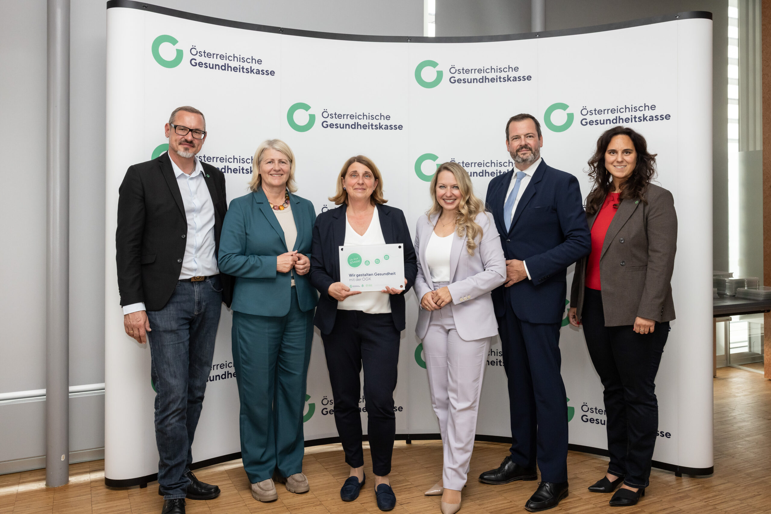 Österreichische Gesundheitskasse: Sechs Personen stehen vor einem Banner mit dem Logo der ÖGK.